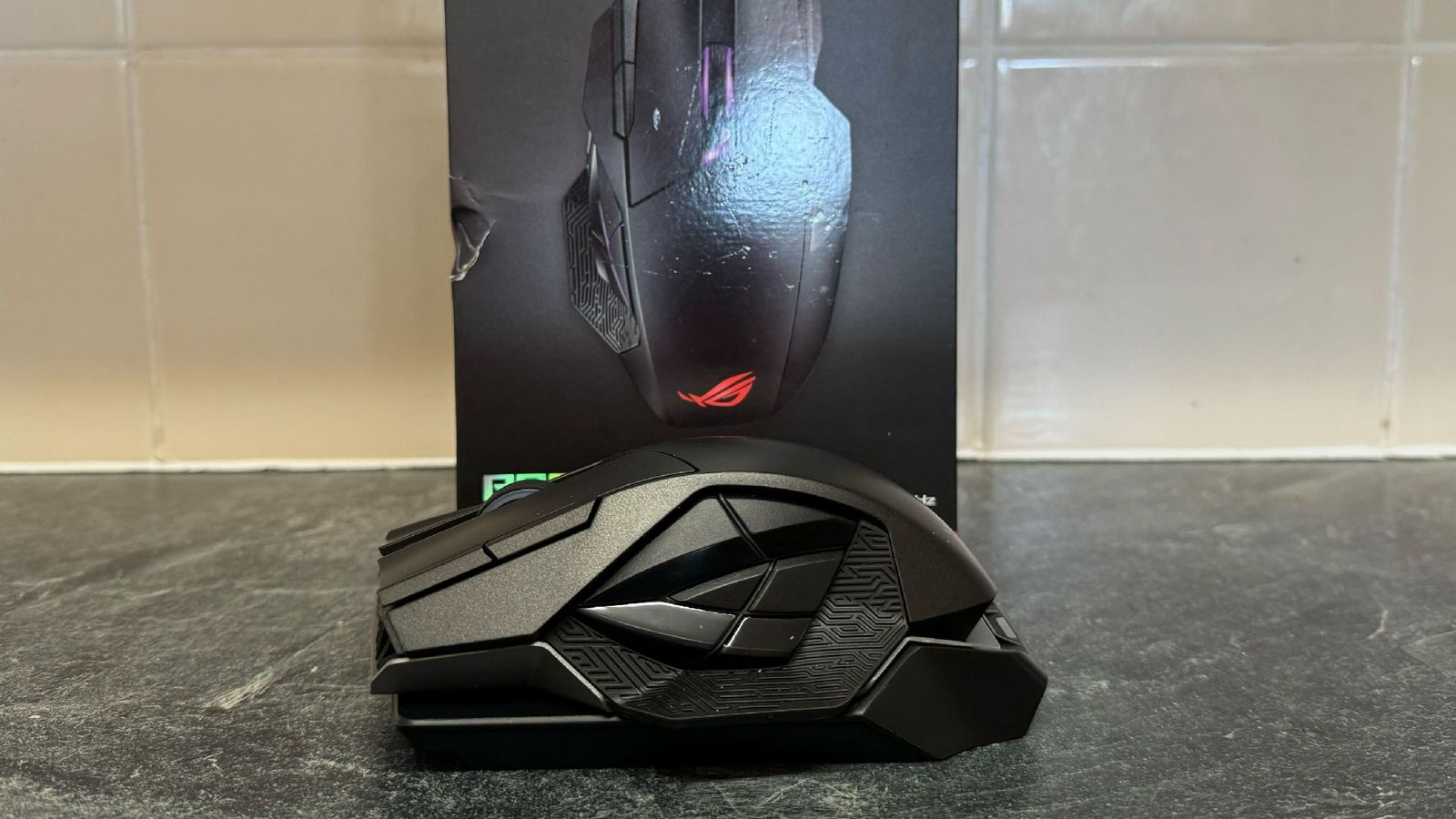 Side view of the ASUS ROG Spatha X in front of its box and a tiled wall