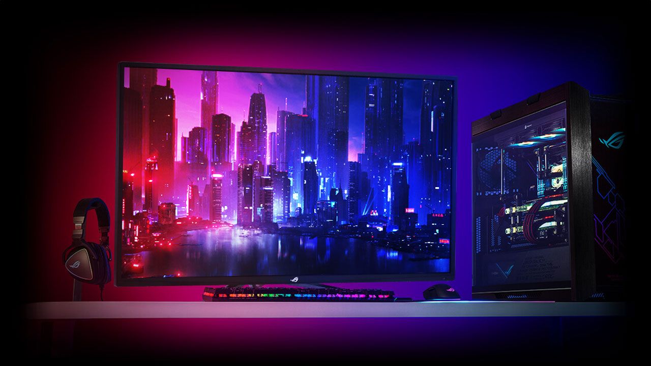 A large 43-inch monitor with a city landscape lit up in red, pink, and blue on the display to match its real life surroundings, complete with a headset, PC, keyboard, and mouse.