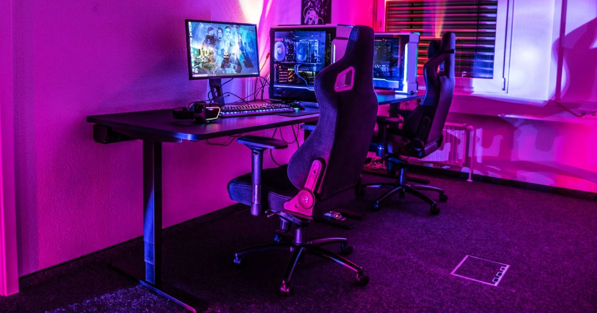 A gaming chair tucked under a desk at a PC setup, with the room bathed in pink light.