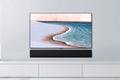 Image of a flatscreen TV featuring a beach on the display on a white shelf with a black soundbar.