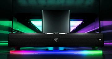 A rectangular black soundbar in front of a subwoofer, with pink, purple, and green lighting underneath it.