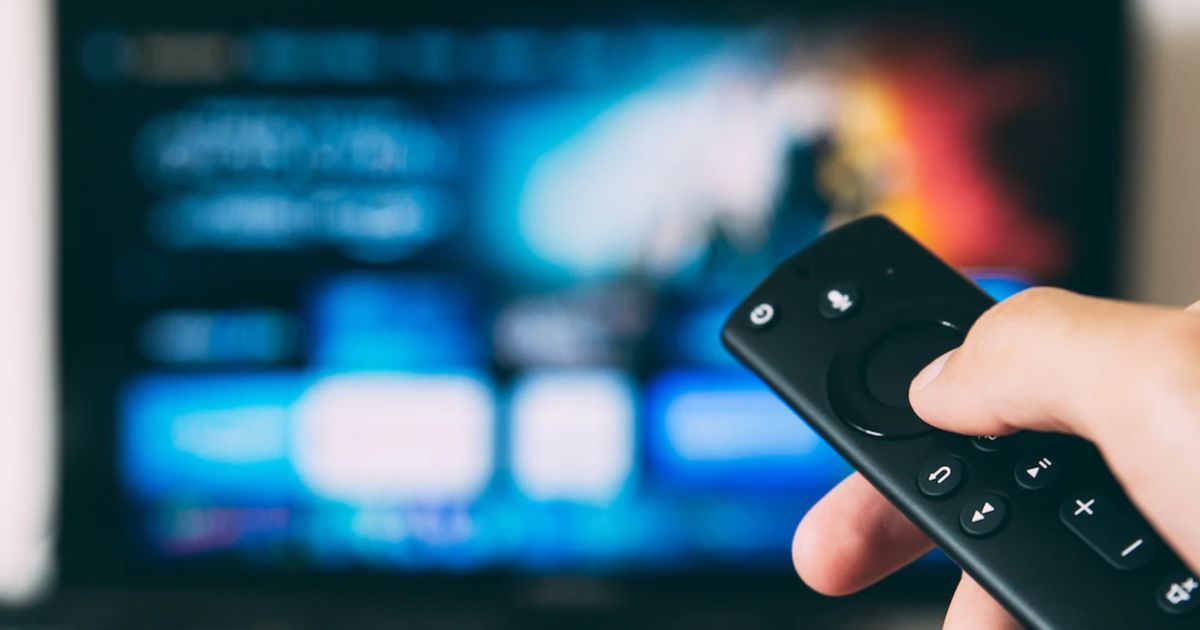 A user holding an Amazon FireTV remote with a blurred TV 