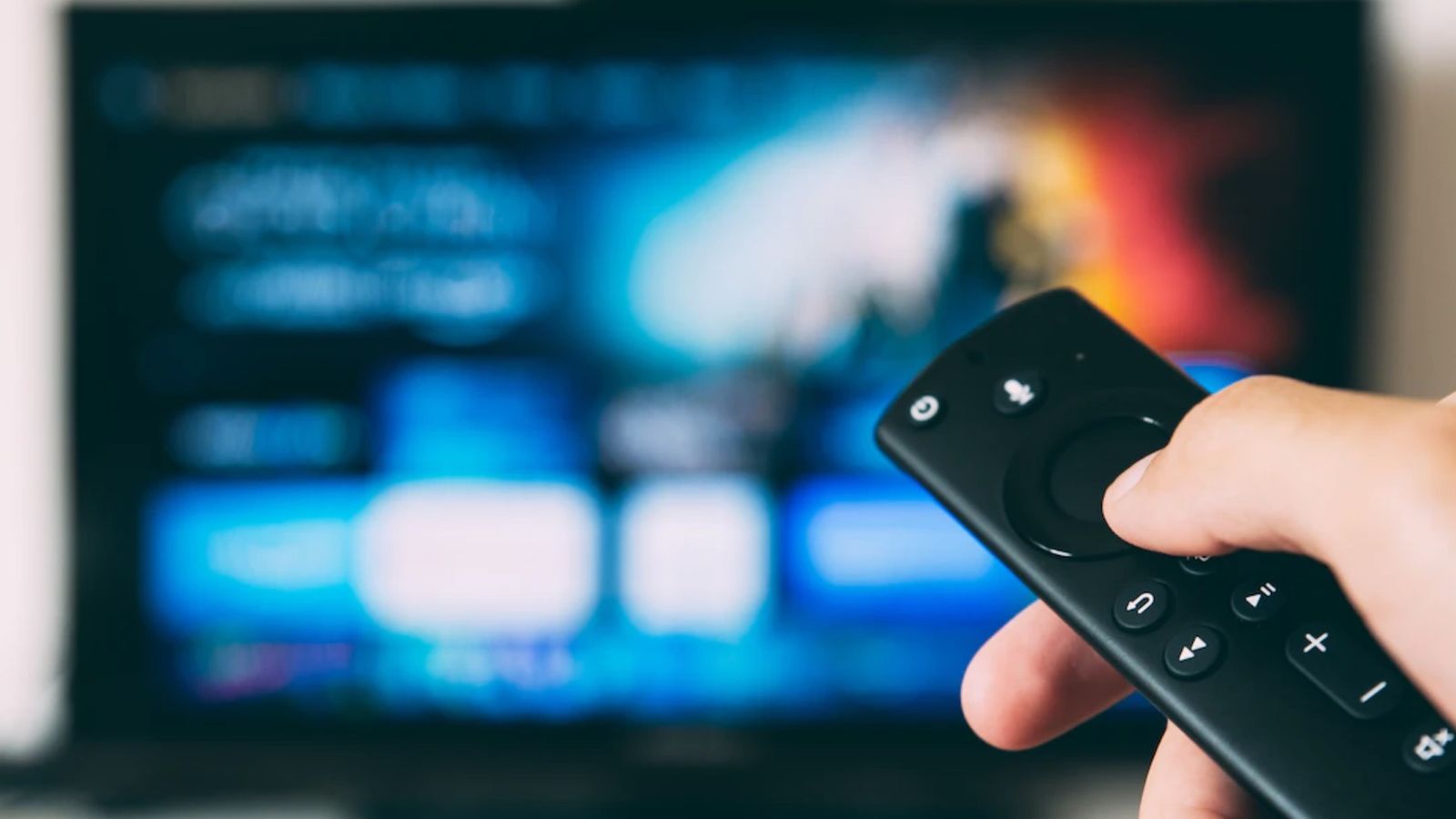 A user holding an Amazon FireTV remote with a blurred TV 